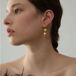 Woman wearing gold heart-shaped earrings against a neutral background