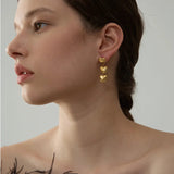 Woman wearing gold heart-shaped earrings against a neutral background