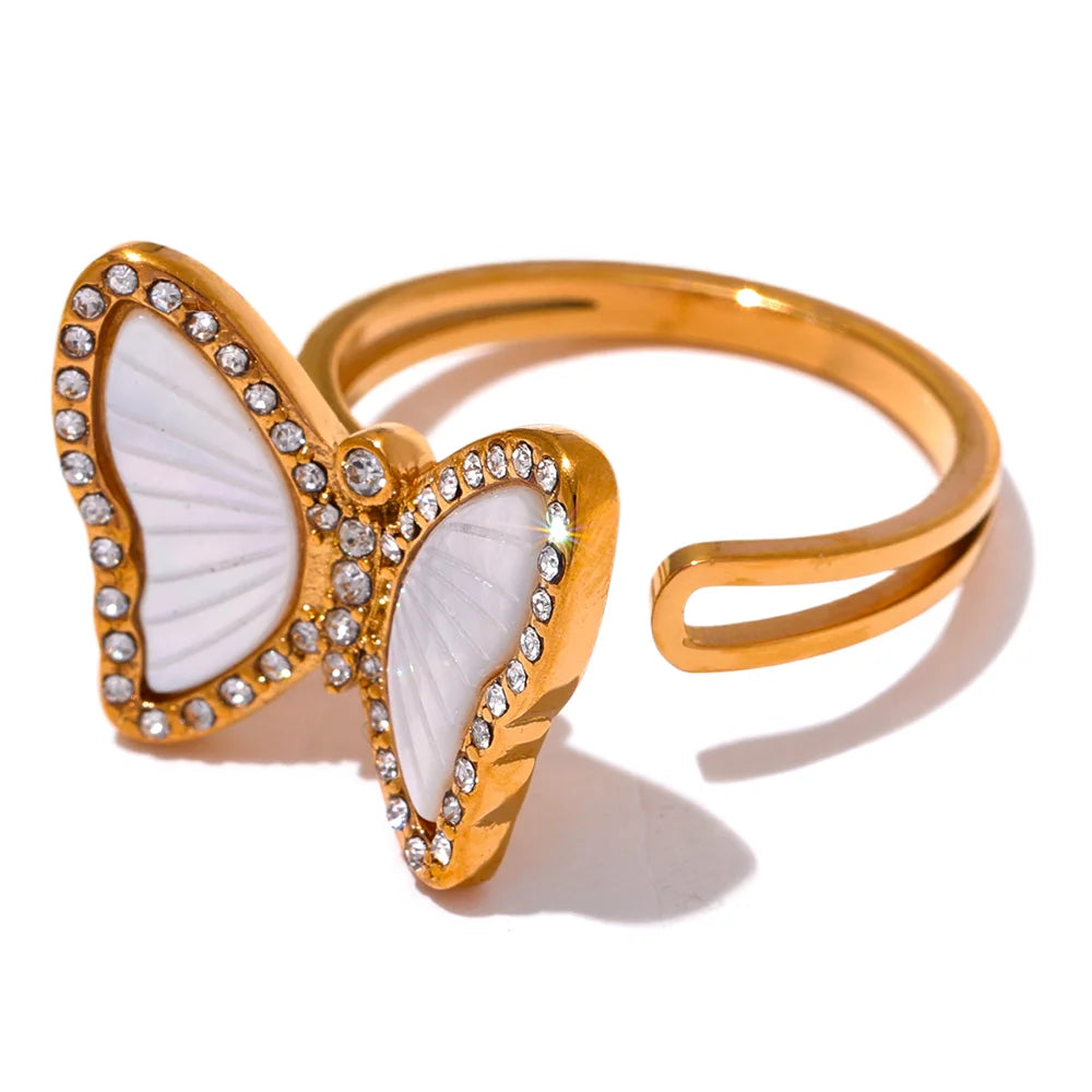 Gold butterfly-shaped ring with white center and clear stones on a white background