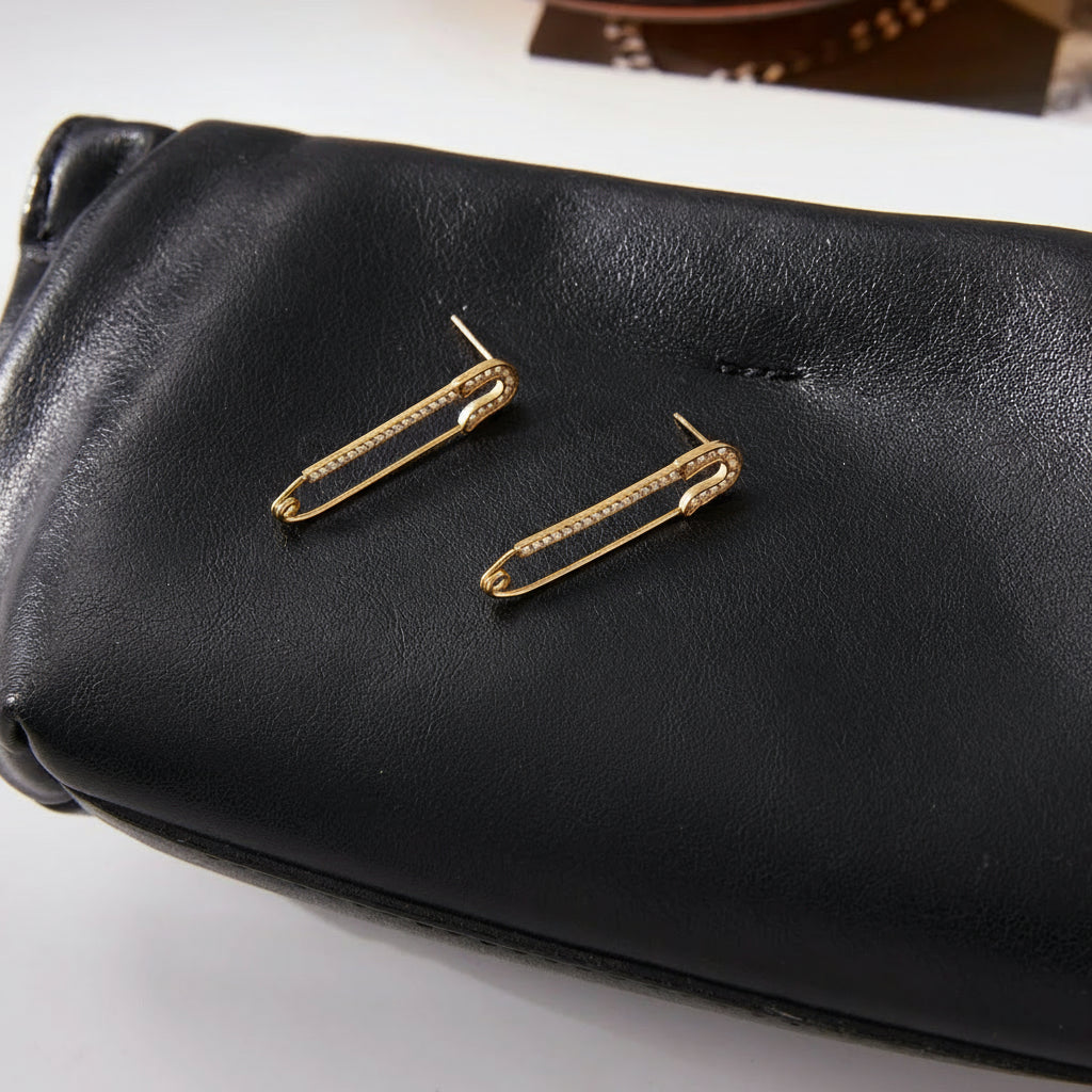 Gold safety pin earrings on a black pouch.