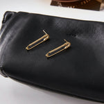 Gold safety pin earrings on a black pouch.