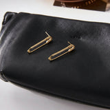Gold safety pin earrings on a black pouch.