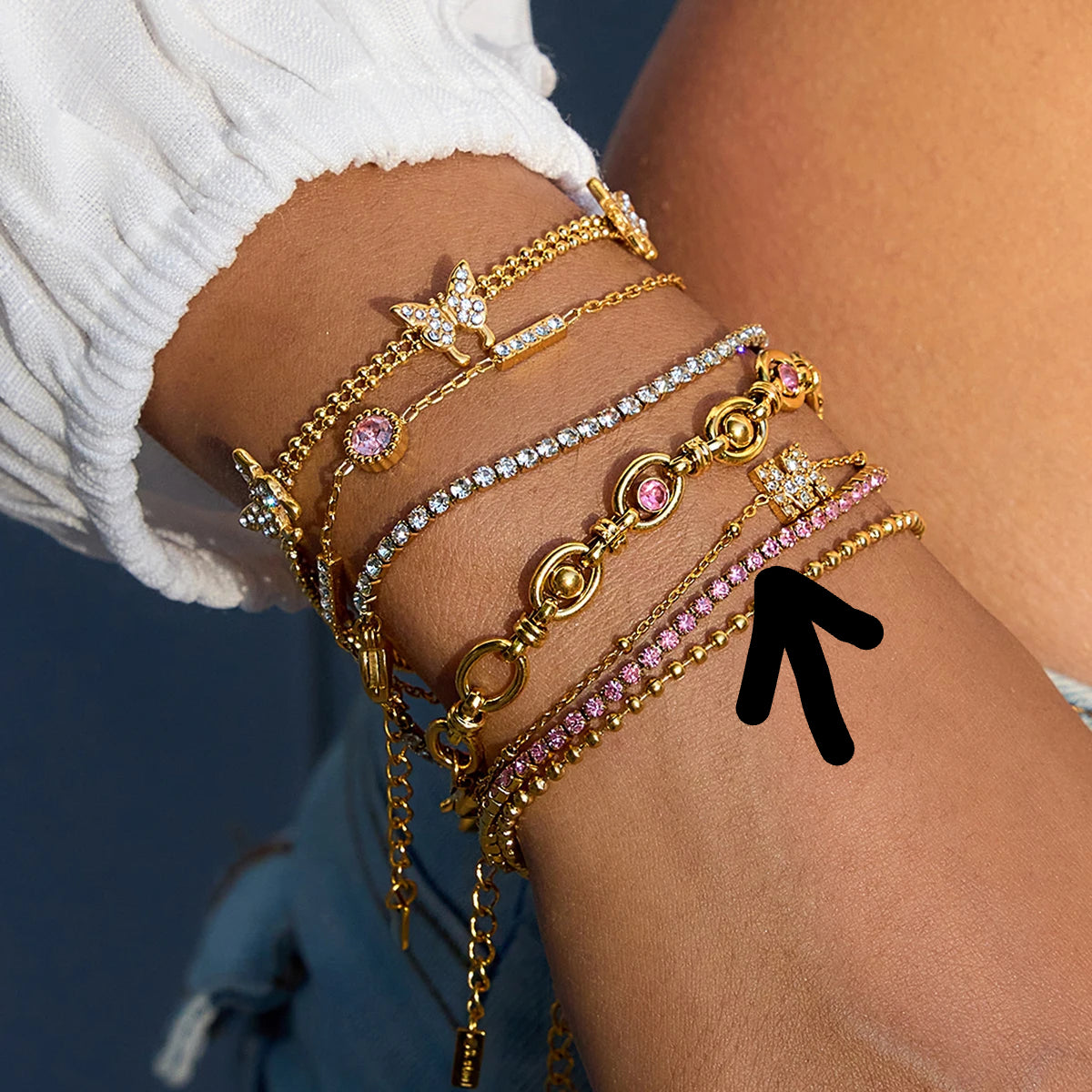 Multiple gold and pink bracelets on a wrist with a blurred background