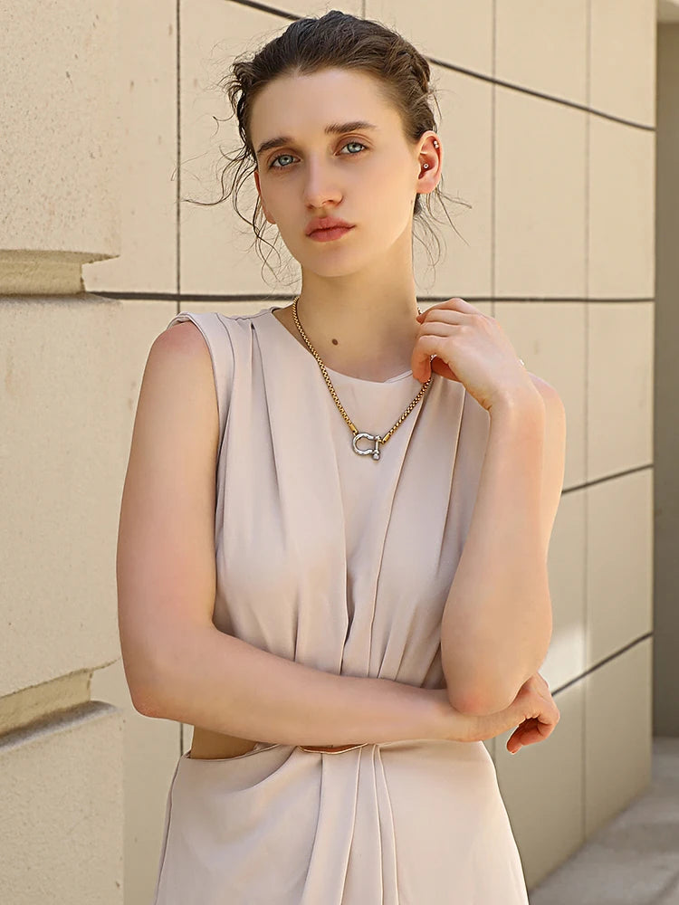Woman wearing a light-colored dress and necklace against a beige wall.