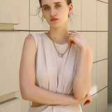 Woman wearing a light-colored dress and necklace against a beige wall.