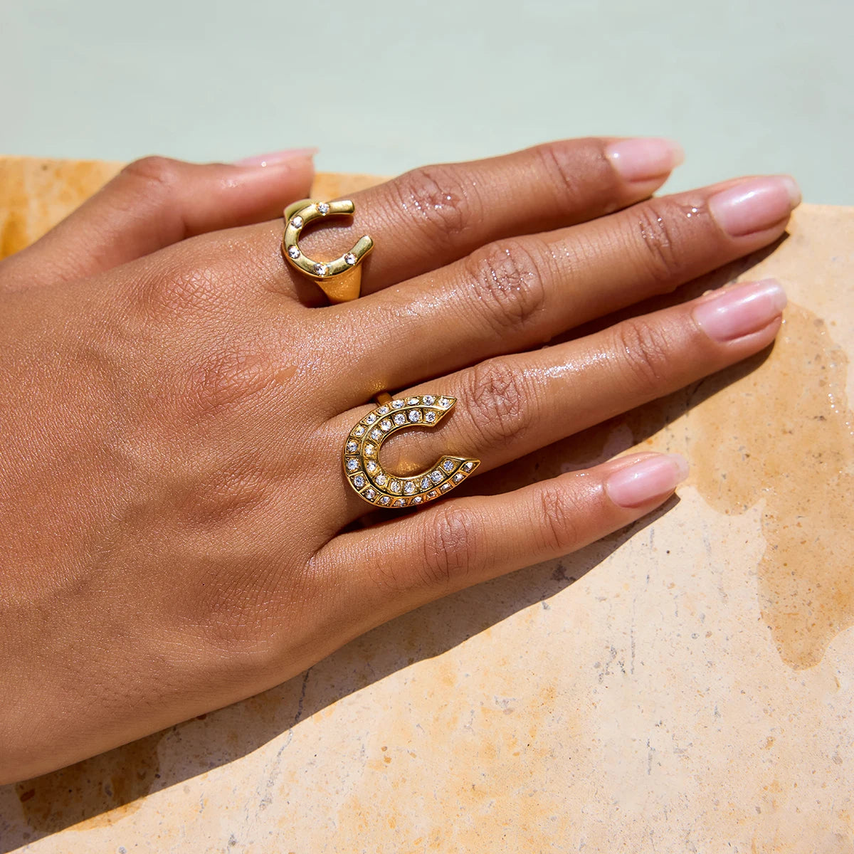 Gold horseshoe-shaped ring with embedded stones on a hand against a neutral background