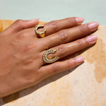 Gold horseshoe-shaped ring with embedded stones on a hand against a neutral background
