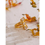 Gold ring with embedded stones on a textured surface with dried flowers
