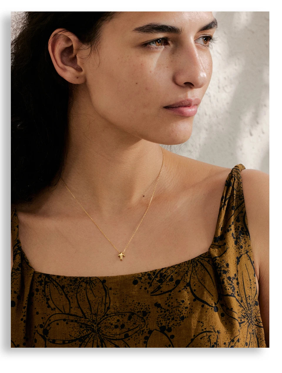 Woman wearing a gold necklace with a small pendant against a neutral background
