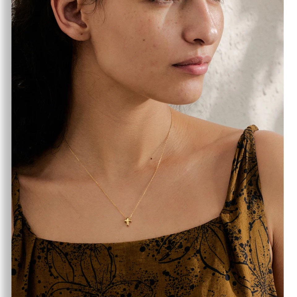 Woman wearing a gold necklace with a small pendant against a neutral background