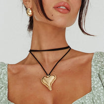 Woman wearing a gold heart pendant necklace with a plain background