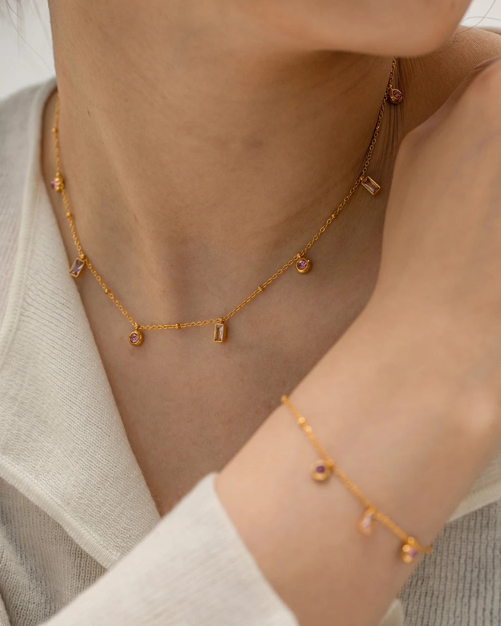 Gold necklace and bracelet on a person wearing a light gray cardigan.