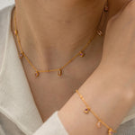 Gold necklace and bracelet on a person wearing a light gray cardigan.