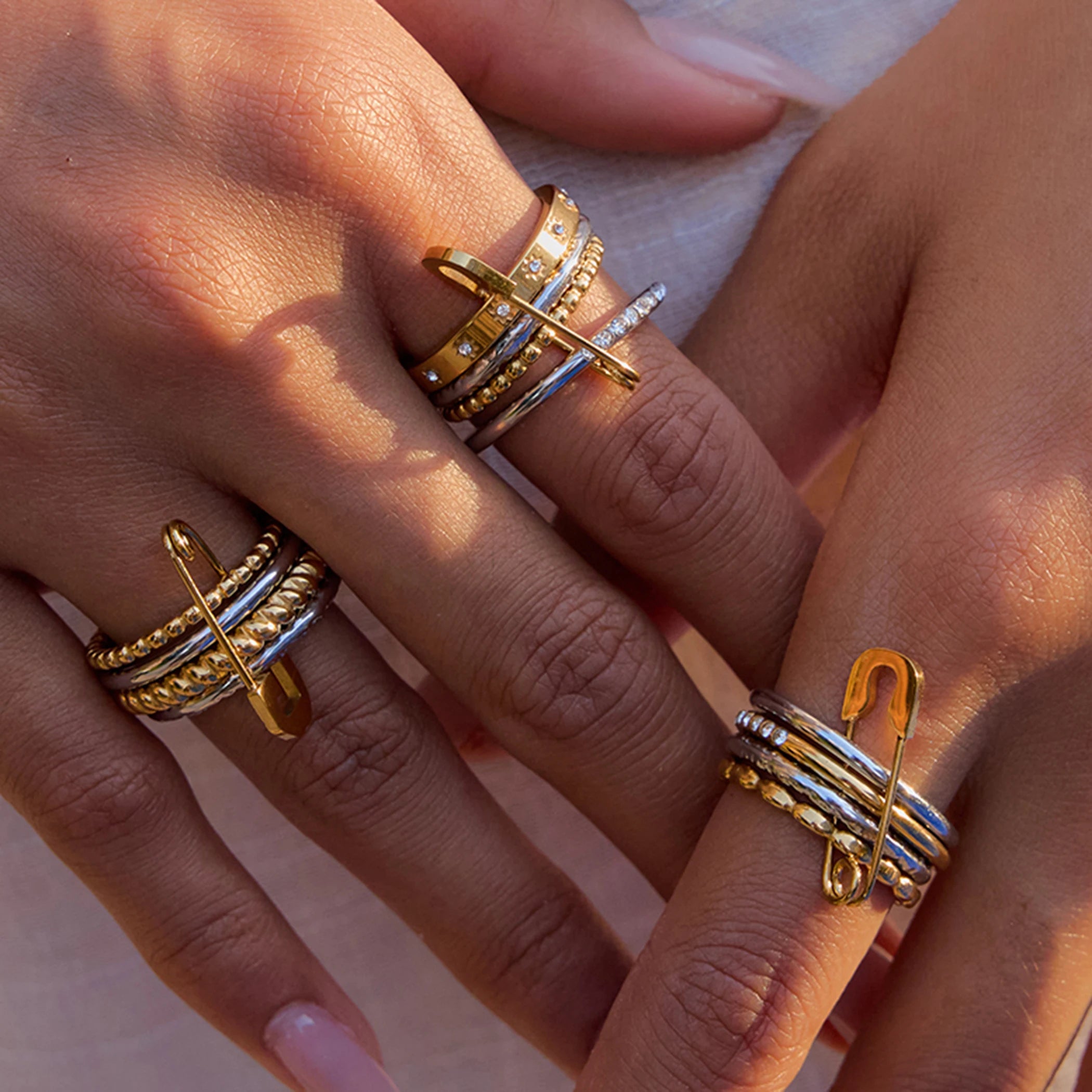 Close-up of hands wearing multiple gold and silver rings on a neutral background