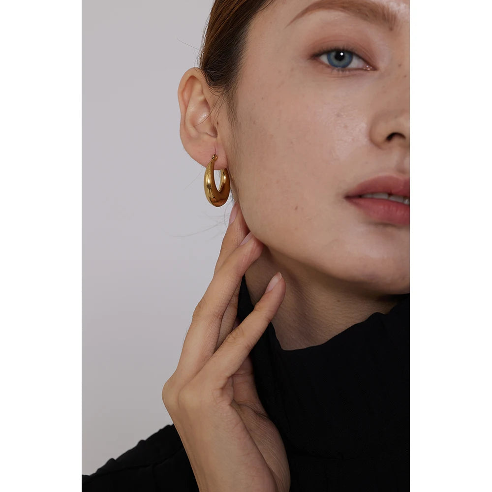 Close-up of a person wearing gold hoop earrings with a neutral background