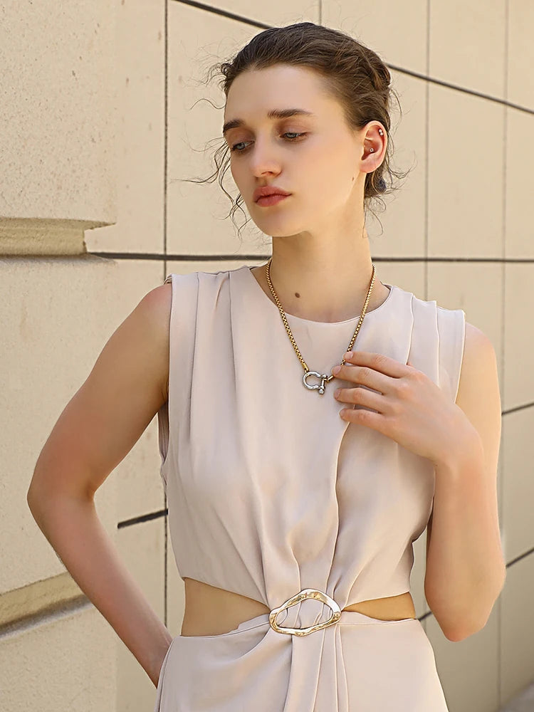 Woman wearing a light-colored dress with a belt against a beige wall.