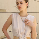 Woman wearing a light-colored dress with a belt against a beige wall.