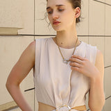 Woman wearing a light-colored dress with a belt against a beige wall.