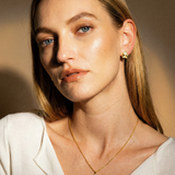 Woman wearing a gold necklace and earring against a warm-toned background