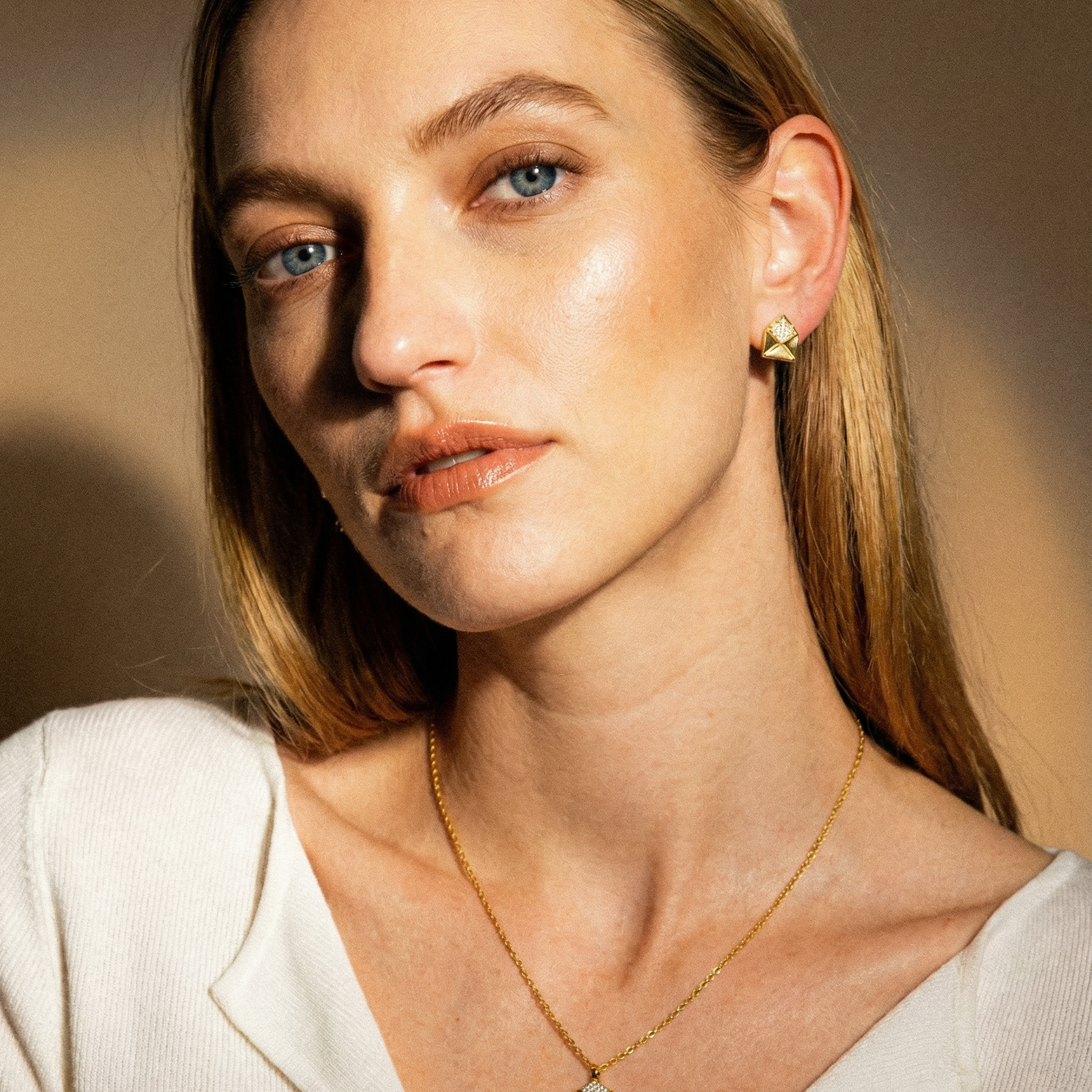 Woman wearing a gold necklace and earring against a warm-toned background