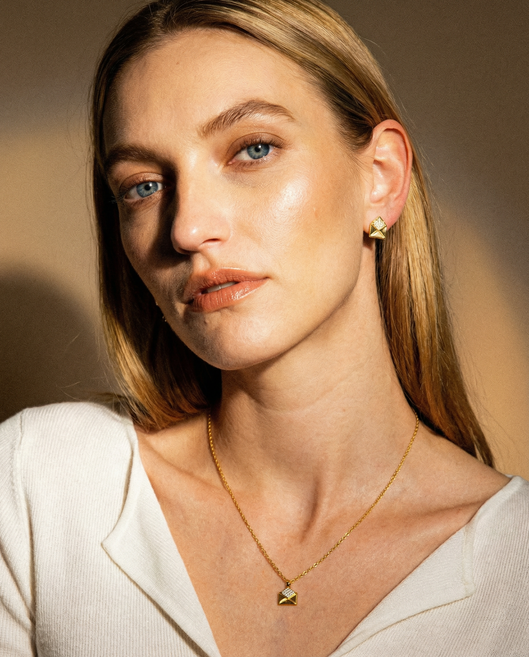Woman wearing a gold necklace and earring against a warm-toned background