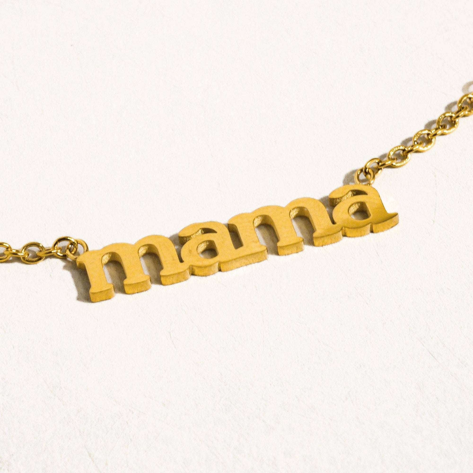 Gold necklace with 'mama' pendant on a white background