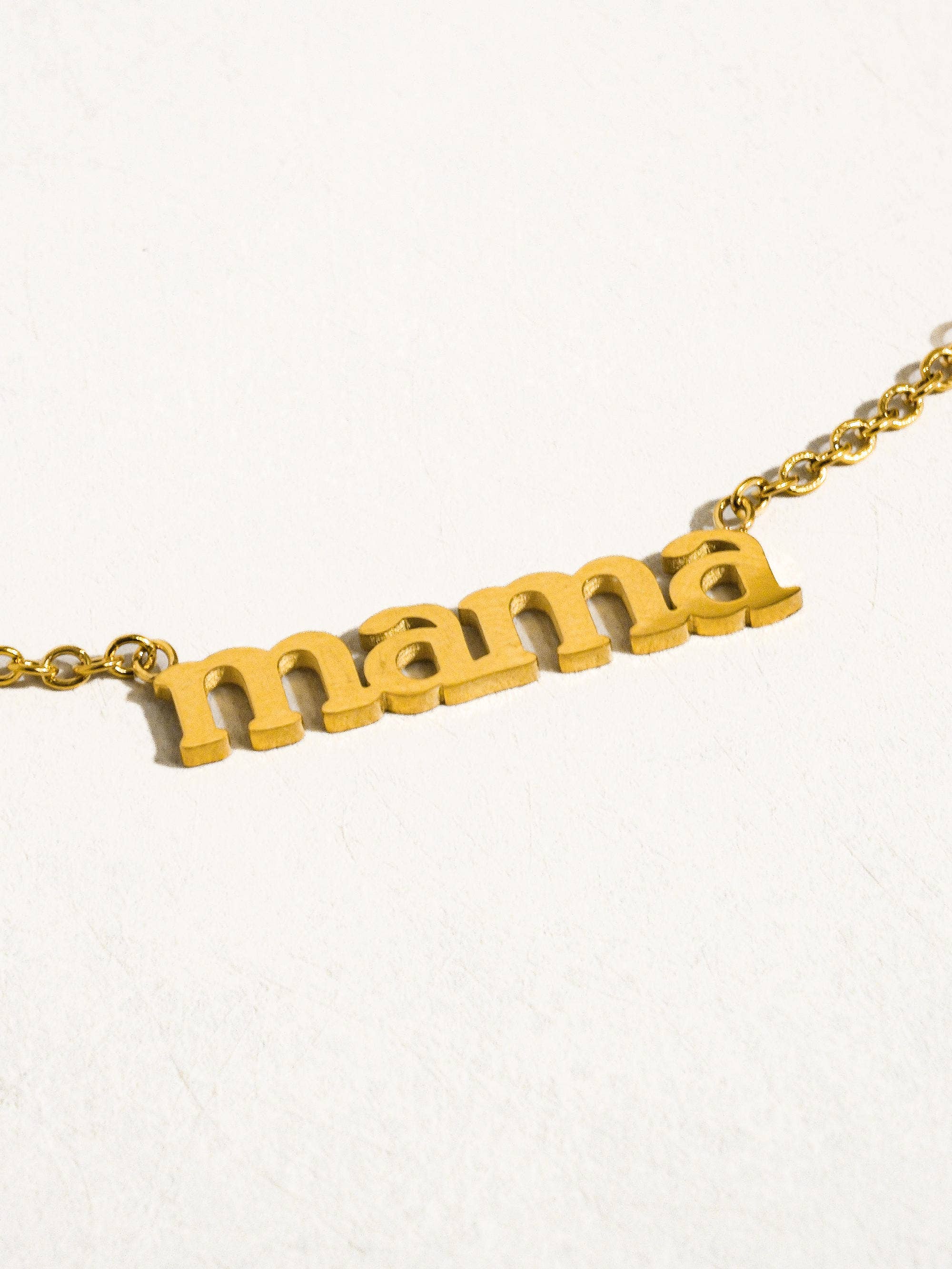 Gold necklace with 'mama' pendant on a white background