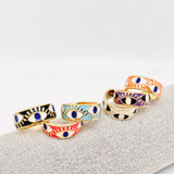 Adjustable gold-plated ring featuring a vibrant blue enamel band with bold evil eye symbols for protection