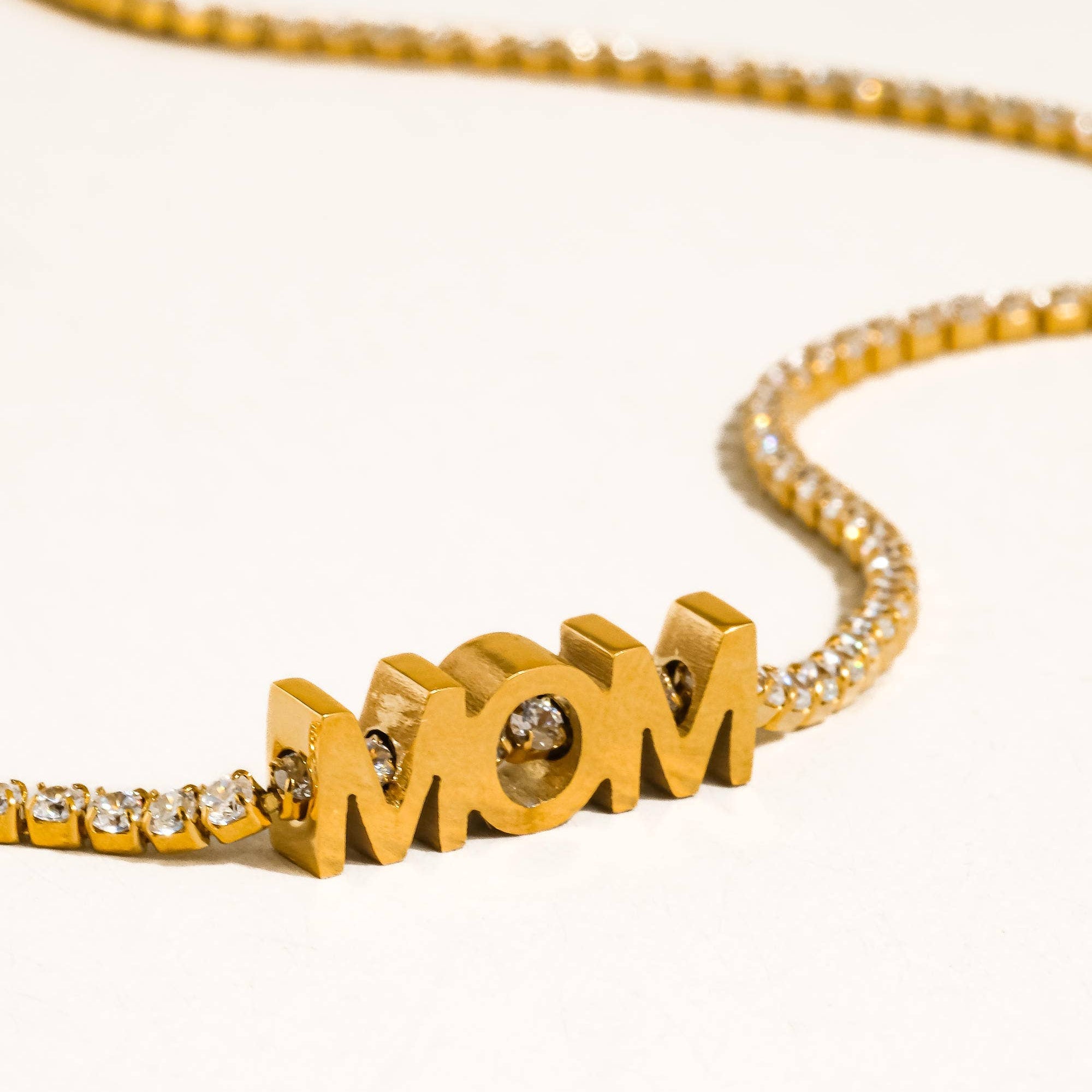 Gold necklace with 'MOM' pendant on a white background