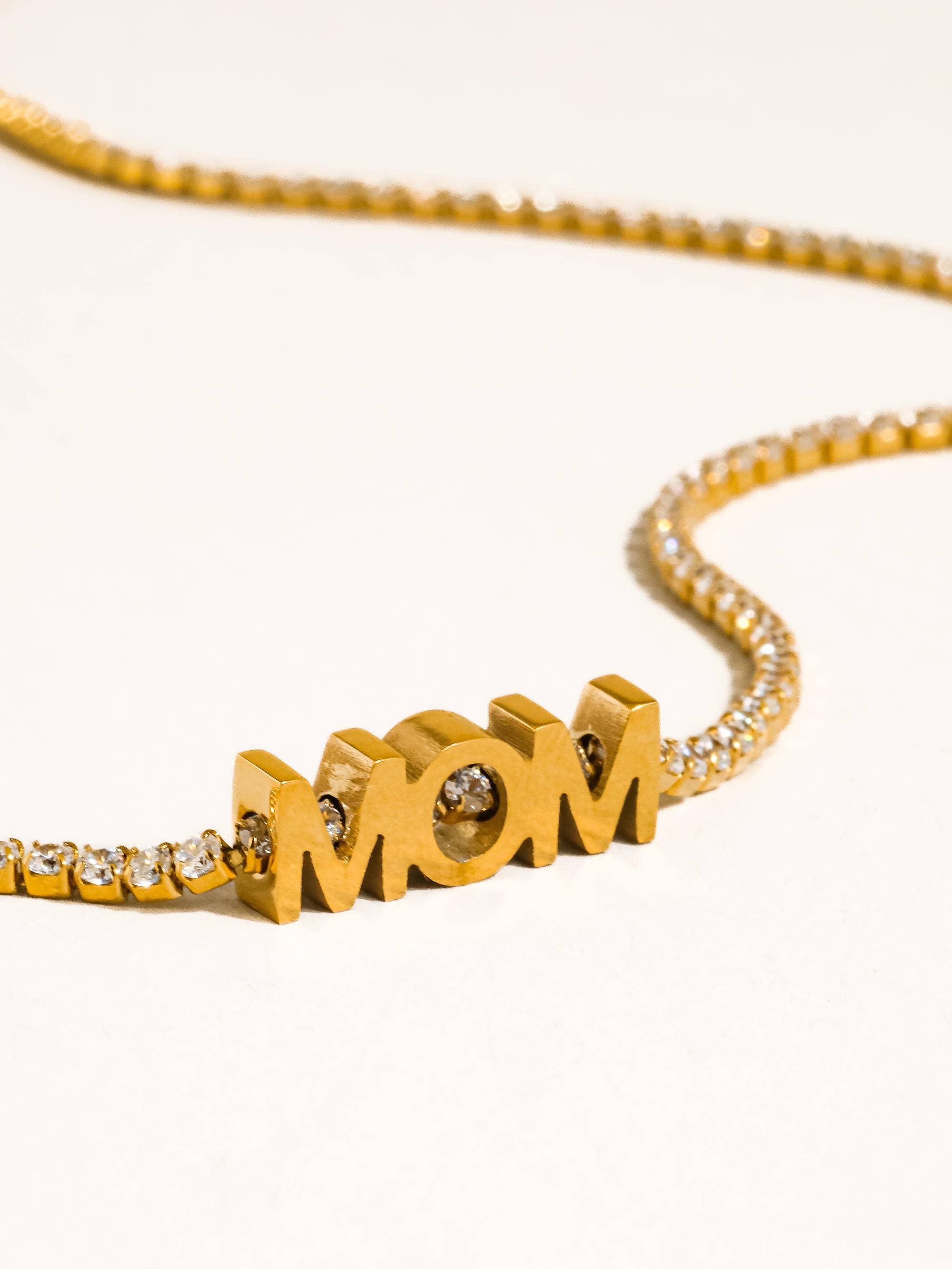 Gold necklace with 'MOM' pendant on a white background