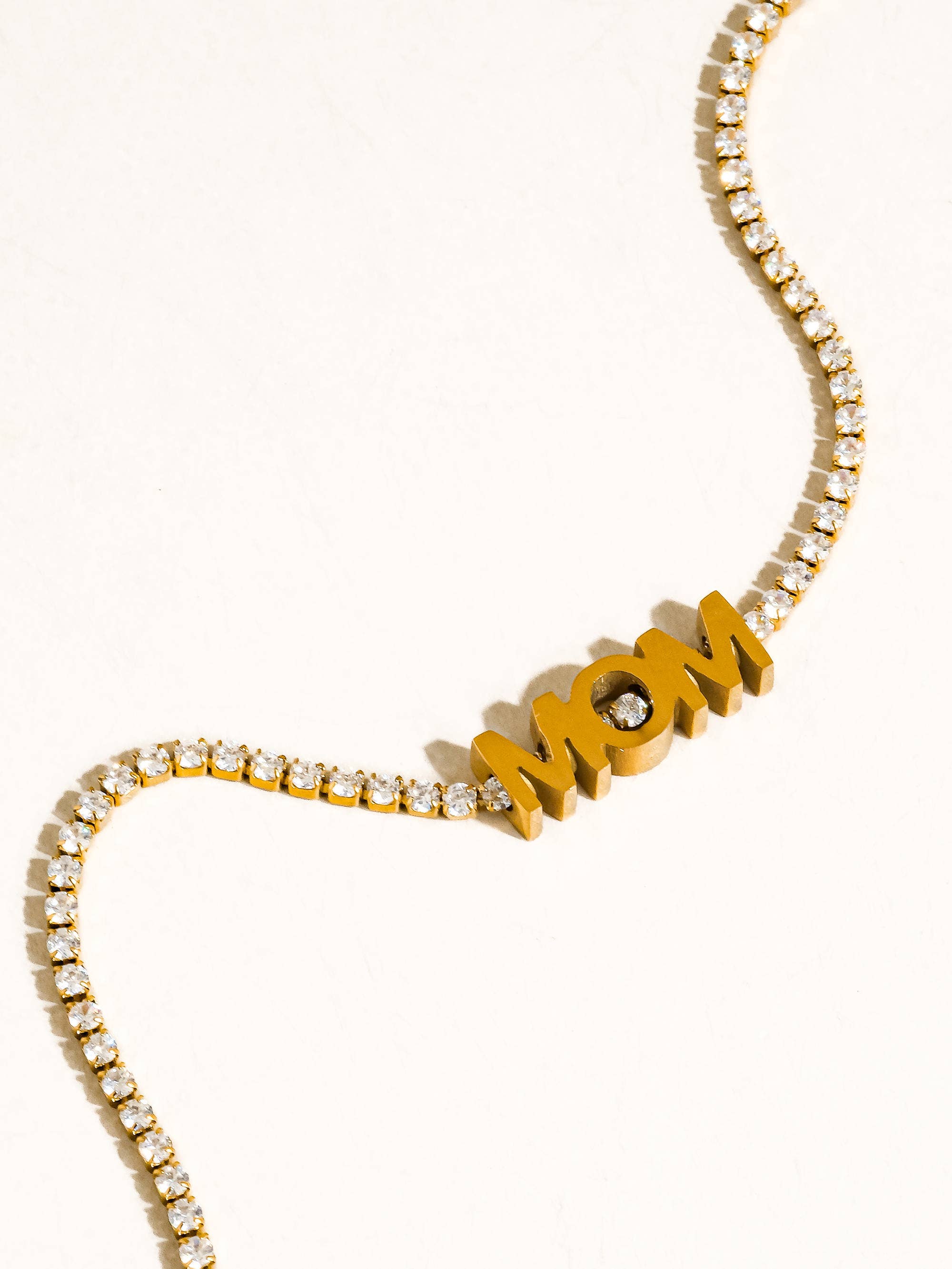 Gold necklace with 'MOM' pendant on a white background