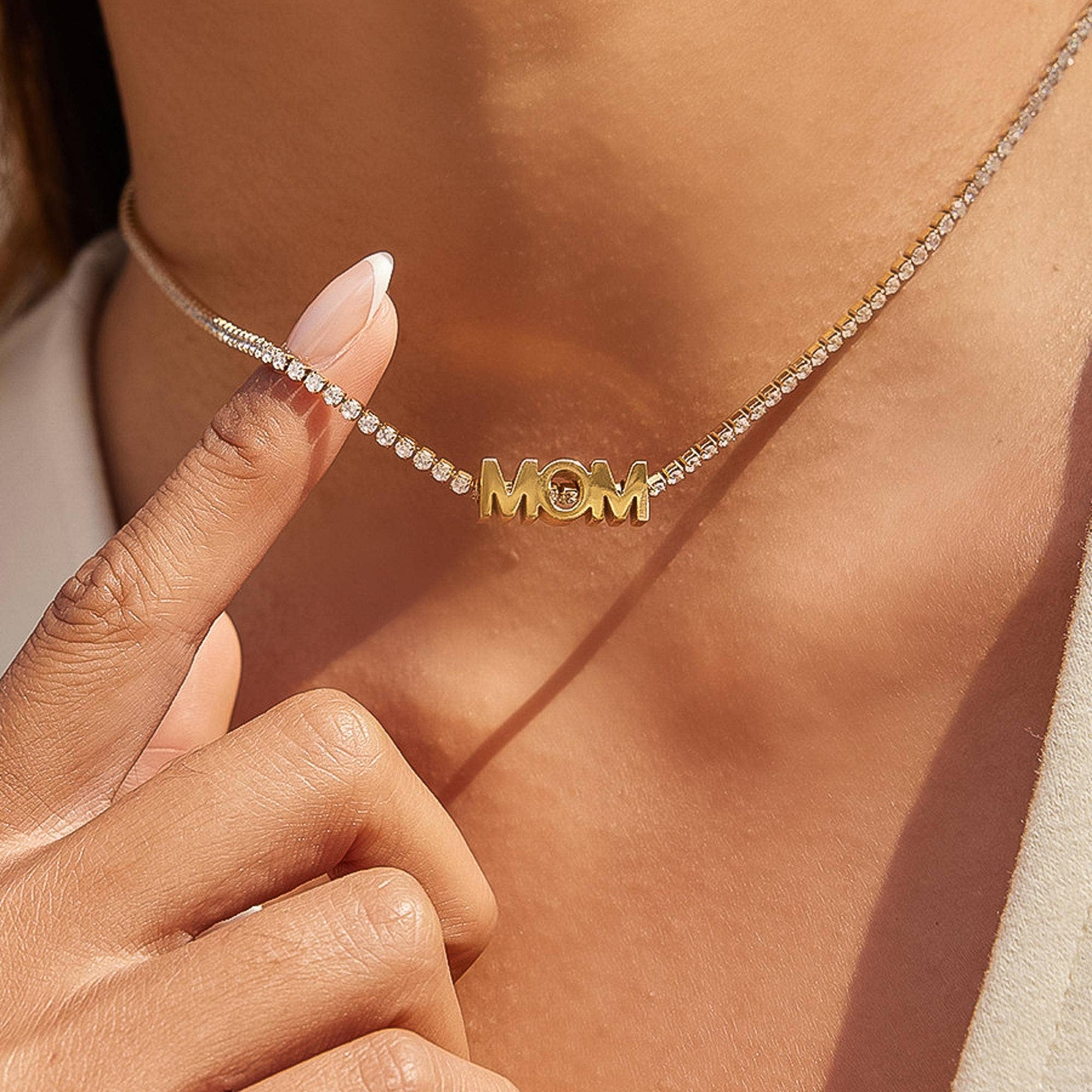 Gold 'MOM' necklace being worn on a person's neck with a close-up of the necklace.