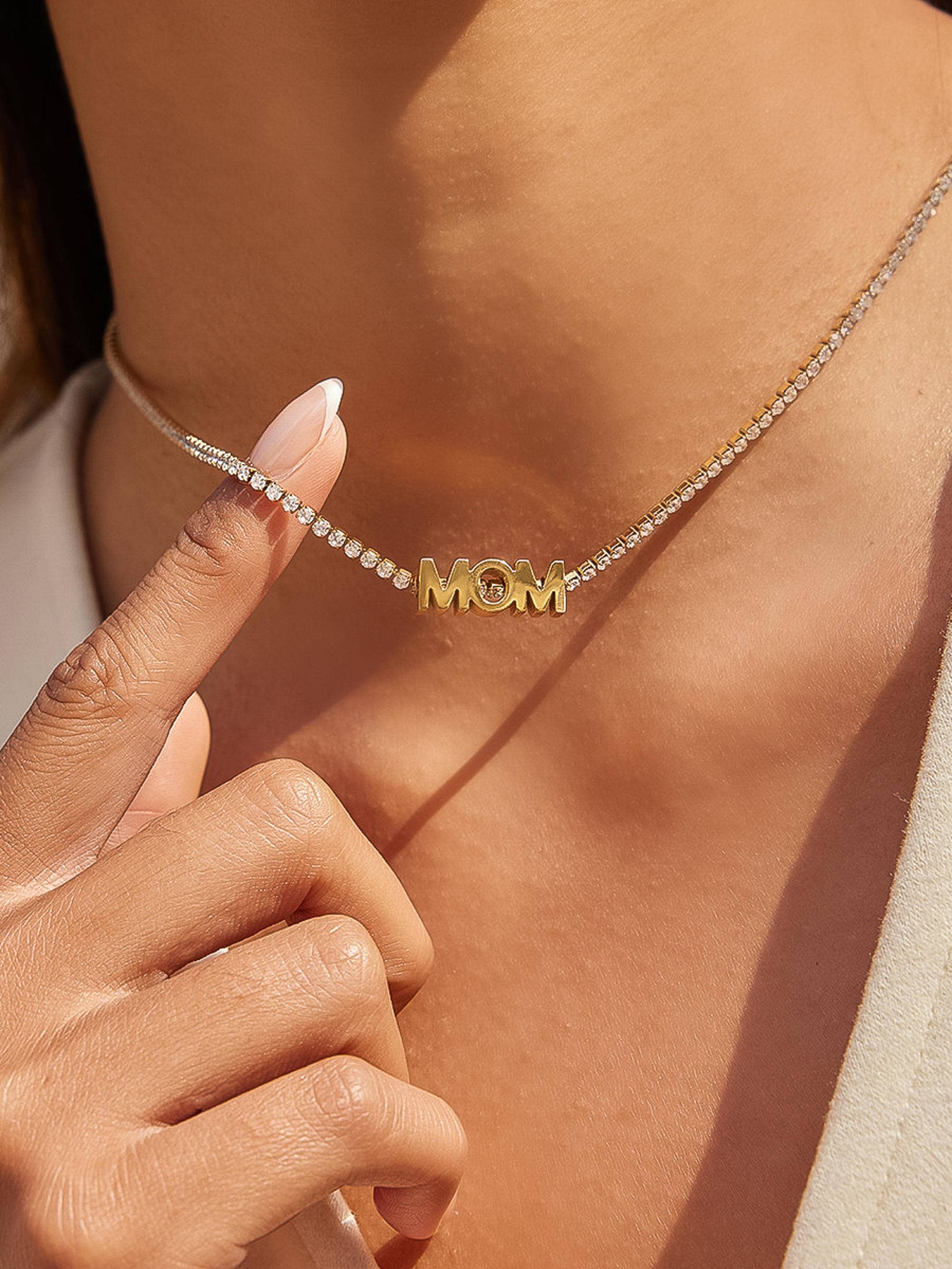 Gold 'MOM' necklace being worn on a person's neck with a close-up of the necklace.
