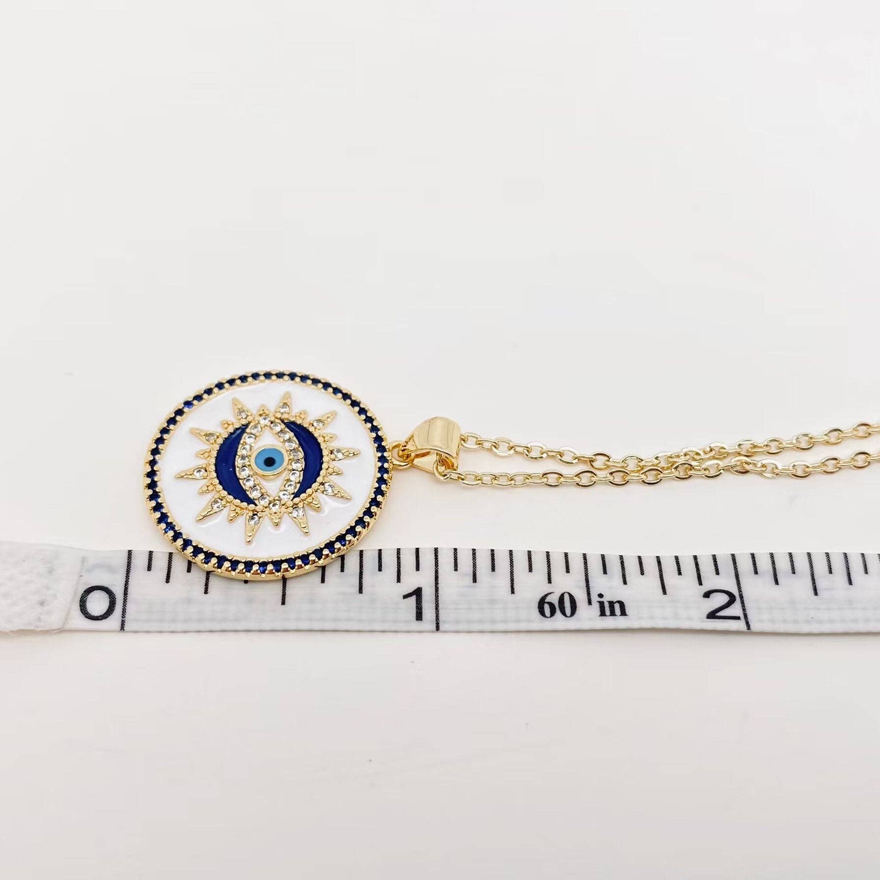 White enamel evil eye necklace featuring a blue stone charm on a gold chain, bringing stylish protection to your everyday look.